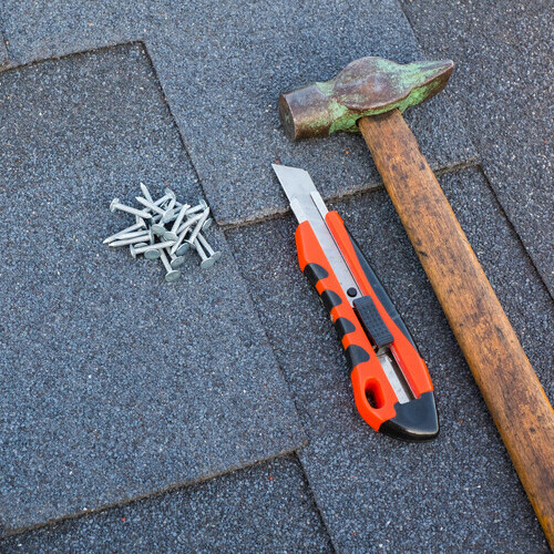 Close up view on asphalt bitumen shingles on a roof  with hammer,nails and stationery knife 